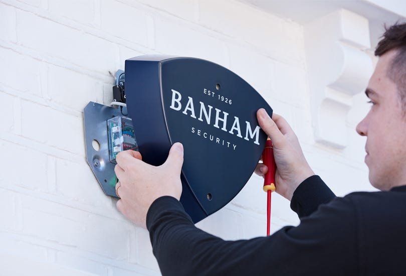 An engineer fitting a Banham burglar alarm system to an external wall.